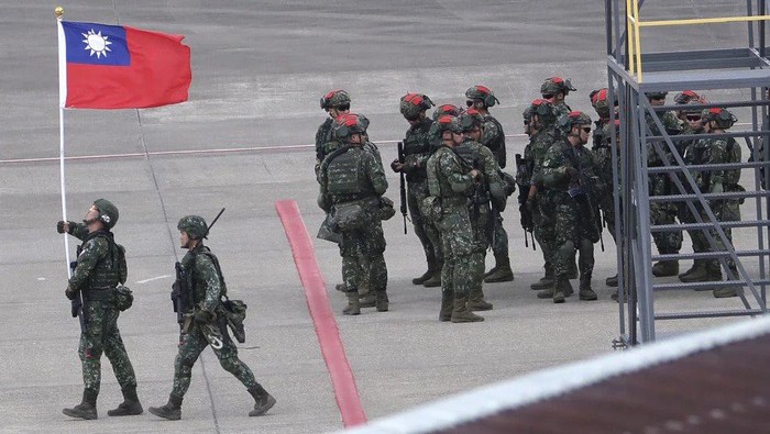 FILE - A Taiwanese soldier holds a Taiwan national flag near a group of soldiers with red markings on their helmets to play the role of an enemy during the annual Han Kuang military exercises simulating an attack on an airfield at Taoyuan International Airport in Taoyuan, Northern Taiwan, Wednesday, July 26, 2023. Taiwan’s defense ministry says Wednesday, Aug. 2, that it has detained an army officer and several collaborators on suspicion of handing military secrets to China. (AP Photo/Chiang Ying-ying, File)