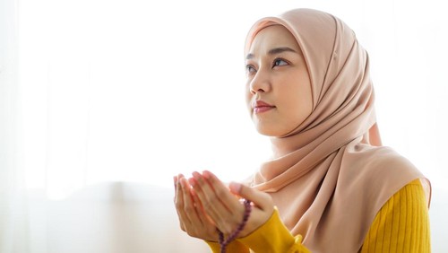 Beautiful Asian young Muslim woman sit on the floor in her house and praying for a holy god - Allah in Islam believe.