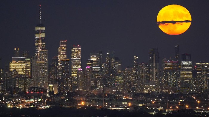 Pesona Supermoon di Atas Cakrawala Kota Manhattan The moon rises through clouds over the skyline of lower Manhattan as seen from West Orange, N.J., Tuesday, Aug. 1, 2023. The first of two supermoons in August graced the skies on Tuesday. A supermoon is broadly defined as a full moon that is closer to the Earth than normal. That makes it appear slightly brighter and bigger in the sky. (AP Photo/Seth Wenig)