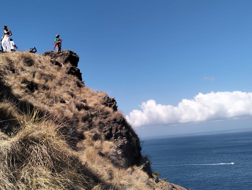 Wisatawan berfoto di sebuah bongkahan batu di Pulau Padar. Topografi curam di belakang batu itu hingga ratusan meter ke bibir pantai di bawahnya. (Amrosius Ardin)
