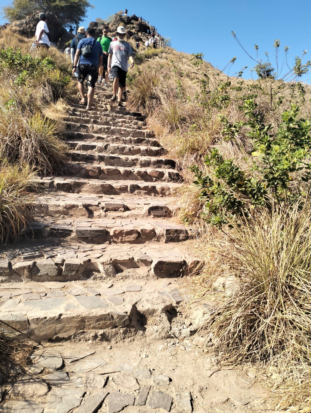 Wisatawan berjalan di jalur tanpa anak tangga menuju puncak Pulau Padar. Wisatawan melewati bongkahan baru dengan tangan berpegangan tali. Persis di samping jalur yang dilalui itu medan curam hingga ratusan meter ke pantai. (Ambrosius Ardin)