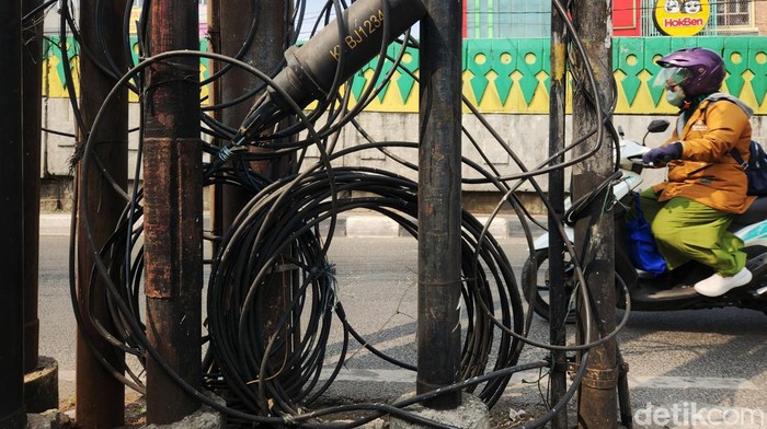 Warga melintas di bawah kabel utilitas yang semrawut di Jalan Ciledug Raya, Cipulir, Jakarta Selatan, Kamis (3/8/2023). Terlihat sejumlah kabel lepas dari ikatan, beberapa menjuntai hingga dapat membahayakan pengendara atau warga yang melintas.