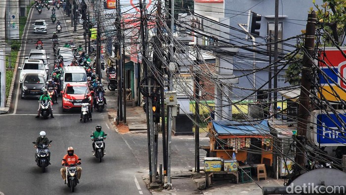 Warga melintas di bawah kabel utilitas yang semrawut di Jalan Ciledug Raya, Cipulir, Jakarta Selatan, Kamis (3/8/2023). Terlihat sejumlah kabel lepas dari ikatan, beberapa menjuntai hingga dapat membahayakan pengendara atau warga yang melintas.