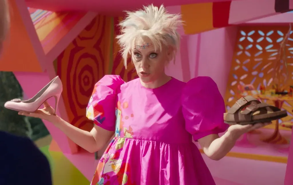 Adegan Film Barbie Weird Barbie yang diperankan Kate McKinnon memegang high heels dan sandal Birkenstock.