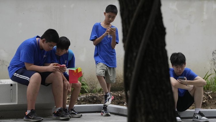 Youths look at their smartphones on the street in Beijing, Thursday, Aug. 3, 2023. Chinas internet watchdog has laid out regulations to curb the amount of time minors spend on their smartphones, in the latest blow to firms such as Tencent and ByteDance which run social media platforms and online games. (AP Photo/Ng Han Guan)