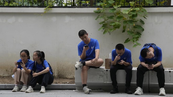 Youths look at their smartphones on the street in Beijing, Thursday, Aug. 3, 2023. Chinas internet watchdog has laid out regulations to curb the amount of time minors spend on their smartphones, in the latest blow to firms such as Tencent and ByteDance which run social media platforms and online games. (AP Photo/Ng Han Guan)
