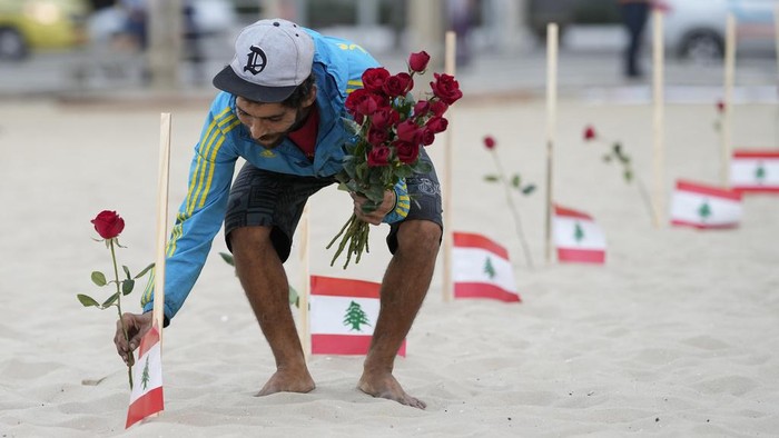 Ratusan Mawar dan Bendera Lebanon Penuhi Pantai Copacabana Brasil A man runs past Lebanese flags placed in honor of those who died in the 2020 Beirut port explosion on the third anniversary of the blast, on Copacabana beach in Rio de Janeiro, Brazil, Friday, Aug. 4, 2023. On Aug. 4, 2020, hundreds of tons of ammonium nitrate exploded at the Beirut port, killing hundreds and injuring thousands. (AP Photo/Silvia Izquierdo)