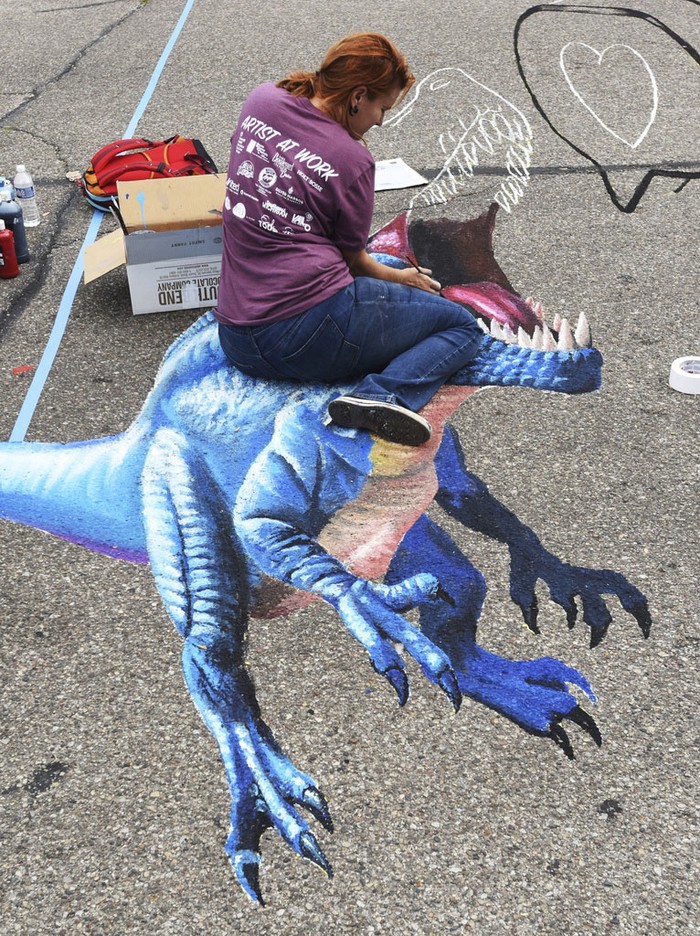 Naomi Haverland, of Titusville, Fla., joins artists as they work on chalk murals, Saturday, Aug. 5, 2023, during the annual Chalk The Block in downtown St. Joseph, Mich. (Don Campbell/The Herald-Palladium via AP)