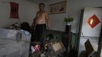 Seorang warga memeriksa barang-barang yang bisa diselamatkan dari rumahnya usai diterjang banjir. Seisi rumahnya penuh lumpur dengan sebagiannya rusak.