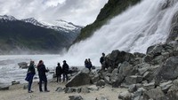 Hamparan abu-abu, putih, dan biru yang terjal, gletser dipenuhi oleh helikopter wisata dan menarik pengunjung dengan kayak, kano, dan berjalan kaki.  