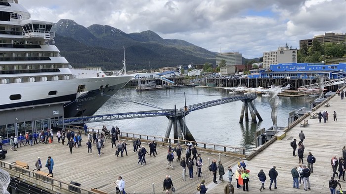 People mill about on the sea walk along which cruise ships dock on June 12, 2023, in downtown Juneau, Alaska. Buses stand ready to take tourists to activities around town. As the Mendenhall Glacier continues to recede, tourists are flooding into Juneau. A record number of cruise ship passengers are expected this year in the city of about 30,000 people.(AP Photo/Becky Bohrer)