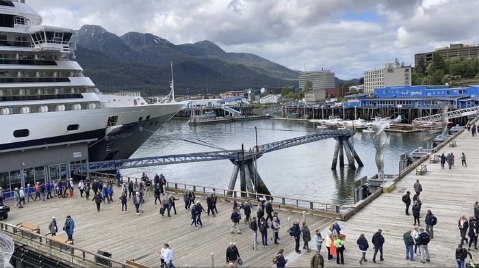 People mill about on the sea walk along which cruise ships dock on June 12, 2023, in downtown Juneau, Alaska. Buses stand ready to take tourists to activities around town. As the Mendenhall Glacier continues to recede, tourists are flooding into Juneau. A record number of cruise ship passengers are expected this year in the city of about 30,000 people.(AP Photo/Becky Bohrer)