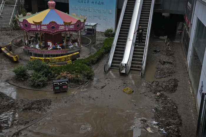 Workers clear mud water from an apartment entrance gate in the aftermath of flood waters from an overflowing river in the Mentougou district on the outskirts of Beijing, Monday, Aug. 7, 2023. Rain continued to pelt northeastern China in the wake of Typhoon Doksuri, as authorities reported more fatalities and missing people while evacuating thousands more. (AP Photo/Andy Wong)