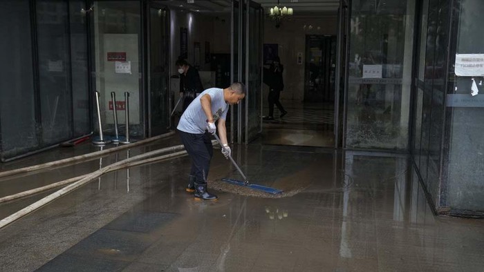 Workers clear mud water from an apartment entrance gate in the aftermath of flood waters from an overflowing river in the Mentougou district on the outskirts of Beijing, Monday, Aug. 7, 2023. Rain continued to pelt northeastern China in the wake of Typhoon Doksuri, as authorities reported more fatalities and missing people while evacuating thousands more. (AP Photo/Andy Wong)