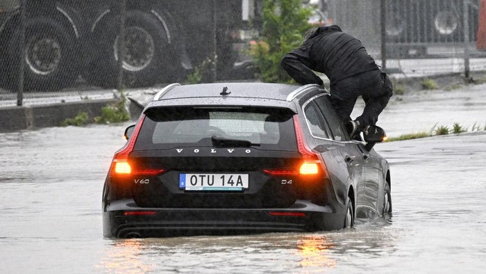 A man climbs out of a car which got stuck at a flooded roundabout in Arlöv, along the E6 road outside Malmö, southern Sweden, Monday, Aug. 7, 2023. Stormy weather across the Baltic Sea region is causing airport delays, suspended ferry service, minor power outages and lots of rain. (Johan Nilsson/TT News Agency via AP)