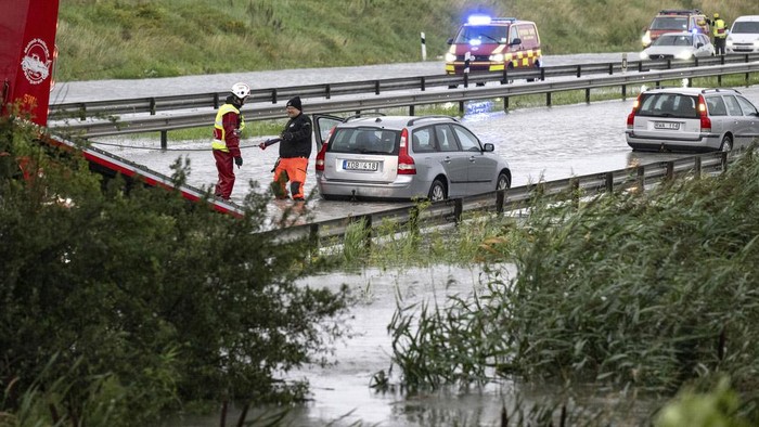 A man climbs out of a car which got stuck at a flooded roundabout in Arlöv, along the E6 road outside Malmö, southern Sweden, Monday, Aug. 7, 2023. Stormy weather across the Baltic Sea region is causing airport delays, suspended ferry service, minor power outages and lots of rain. (Johan Nilsson/TT News Agency via AP)