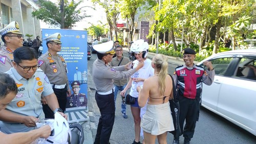Momen polisi dan Jasa Raharja membagikan helm dan kaus kepada WNA saat kampanye keselamatan berlalu lintas di Jalan Raya Legian, Kecamatan Kuta, Kabupaten Badung, Bali, Selasa (8/8/2023). (I Wayan Sui Suadnyana/detikBali)