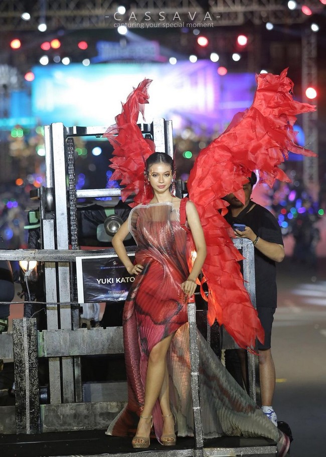 Yuki Kato tampil merah membara di sesi karnaval malam hari. Aktris 28 tahun ini mengenakan gaun bergradasi dengan material kain lipit transparan. Foto: Instagram/@cassava.photography