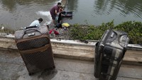Warga mencuci koper dan barang-barang mereka yang tertutup lumpur di tepi kanal di distrik Mentougou di pinggiran Beijing, China, Senin (7/8/2023).
