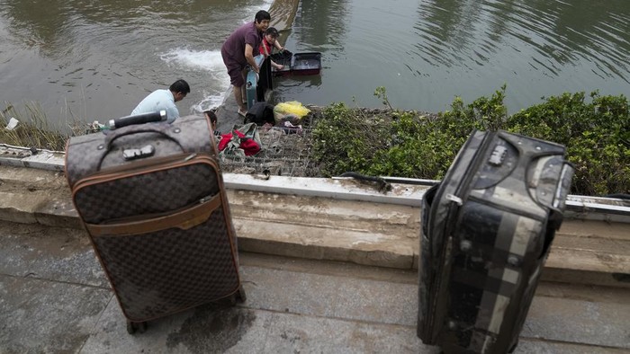 Residents wash their belongings on a bank of a canal clogged with flood debris in the Mentougou district on the outskirts of Beijing, Monday, Aug. 7, 2023. Rain continued to pelt northeastern China in the wake of Typhoon Doksuri, as authorities reported more fatalities and missing people while evacuating thousands more. (AP Photo/Andy Wong)