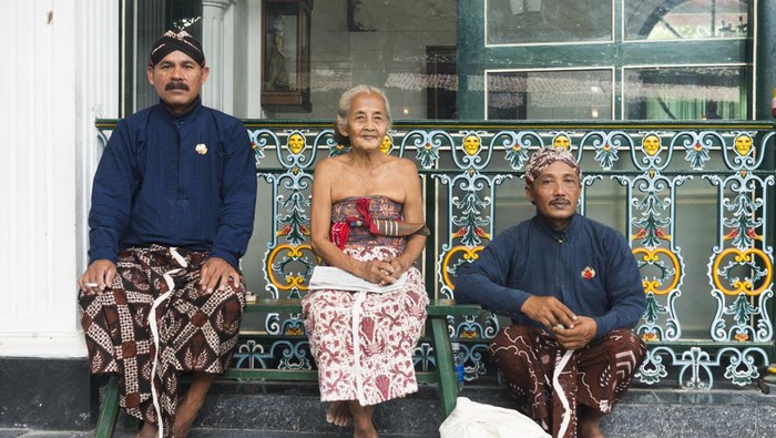 Yogyakarta, Indonesia - April 6, 2015: Three Javanese people wearing traditional clothing sit outside during a break while working at the Sultans Palace in Java, which is also called the Kraton. The two men wear head cloths and sarongs. The senior woman who sits in the middle wears a light colored sarong.
