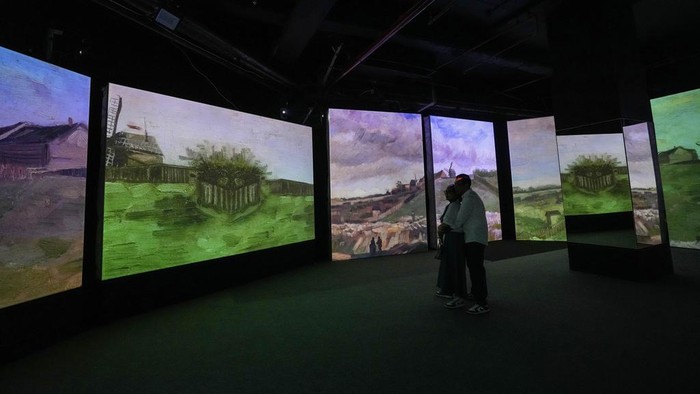 A couple watch visual animated montage of notable works by artist Vincent Van Gogh at the 