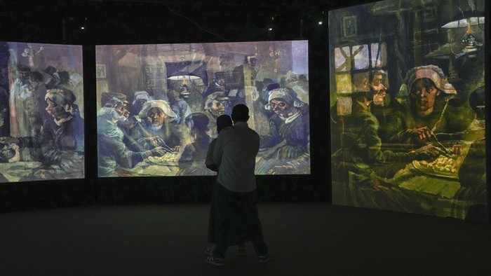 A couple watch visual animated montage of notable works by artist Vincent Van Gogh at the 