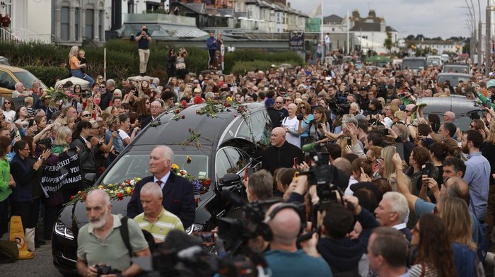 Ribuan Penggemar Melepas Sinead O'Connor ke Peristirahatan Terakhir Fans of Sinead O'Connor line the street as her funeral cortege passes through her former hometown of Bray, Co Wicklow, Ireland, Tuesday, Aug. 8, 2023. OβConnorβs family invited the public to line the waterfront in Bray on Tuesday as her funeral procession passes by. Fans left handwritten notes outside her former home, thanking her for sharing her voice and her music. (Liam McBurney/ PA via AP)