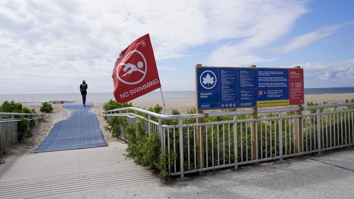 Workers with the New York City Department of Parks and Recreation plant a red flag warning visitors swimming is prohibited on Rockaway beach, Tuesday, Aug. 8, 2023, in the Queens borough of New York. A woman was critically injured when a shark bit her on the leg while she was swimming at a New York City beach, officials said. Rockaway Beach was closed to swimming and surfing on Tuesday as a precaution. (AP Photo/Mary Altaffer)