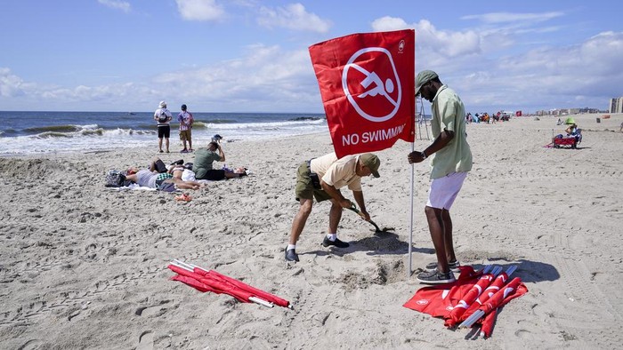 Workers with the New York City Department of Parks and Recreation plant a red flag warning visitors swimming is prohibited on Rockaway beach, Tuesday, Aug. 8, 2023, in the Queens borough of New York. A woman was critically injured when a shark bit her on the leg while she was swimming at a New York City beach, officials said. Rockaway Beach was closed to swimming and surfing on Tuesday as a precaution. (AP Photo/Mary Altaffer)