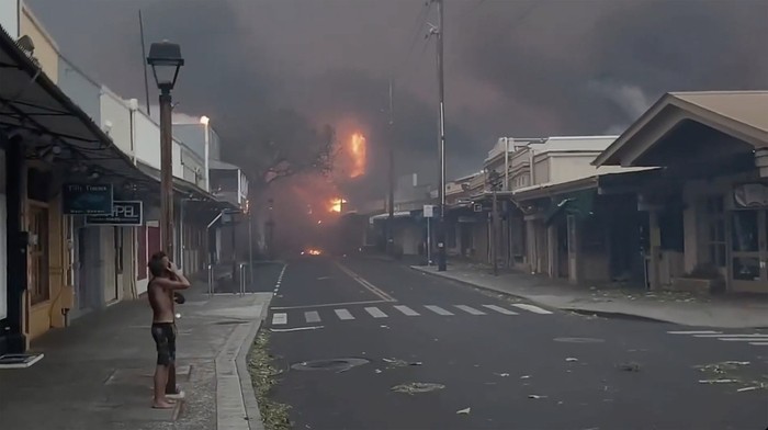 People watch as smoke and flames fill the air from raging wildfires on Front Street in downtown Lahaina, Maui on Tuesday, Aug. 8, 2023. Maui officials say wildfire in the historic town has burned parts of one of the most popular tourist areas in Hawaii. County of Maui spokesperson Mahina Martin said in a phone interview early Wednesday fire was widespread in Lahaina, including Front Street, an area of the town popular with tourists. (Alan Dickar via AP)