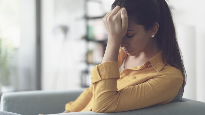 Depressed young woman sitting in the living room at home, she is feeling hopeless and sad