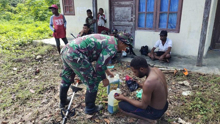 Salah satu personel Satgas Pamtas Statis Yonif 122/TS saat membantu seorang warga dalam karya bakti.