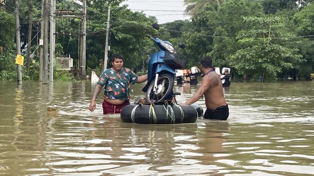 Penduduk setempat mendorong sepeda motor di atas rakit darurat yang terbuat dari ban dalam di jalan yang terendam banjir di Bago, Myanmar, sekitar 80 kilometer (50 mil) timur laut Yangon, Jumat, 11 Agustus 2023. (AP Photo)