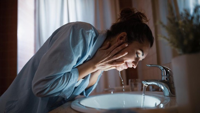 Young smiling woman washing face in the bathroom.