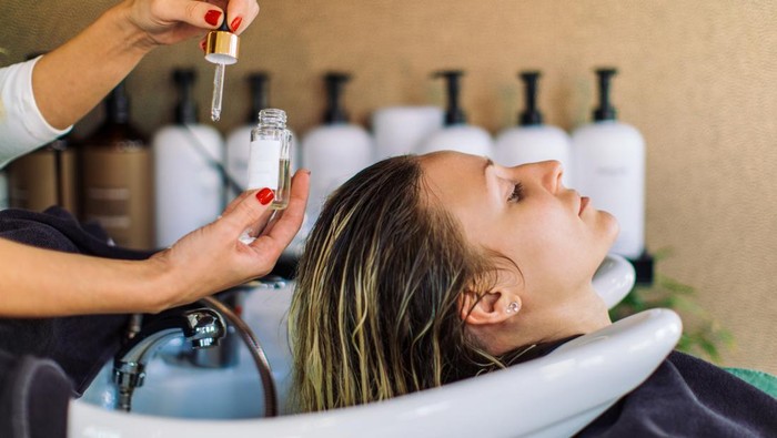 Beautiful young woman getting her hair washed in hair salon. She is relaxing with her eyes closed while the hairdresser massages her scalp and washes her hair with shampoo, hair treatment and water.