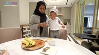 Tibalah saat Rayyanza menaruh topping ke atas pisang panggang. Ia kembali mengenakan seragam chef lengkap supaya makin keren.