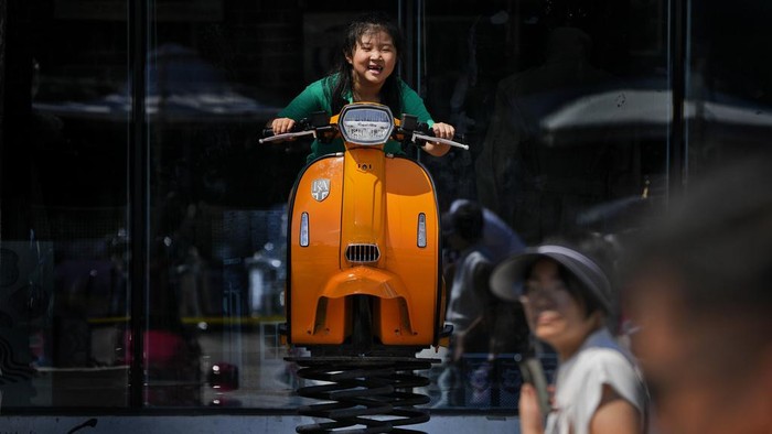 A child enjoys herself on a swing vespa outside a fashion boutique in Beijing, Sunday, Aug. 13, 2023. (AP Photo/Andy Wong)