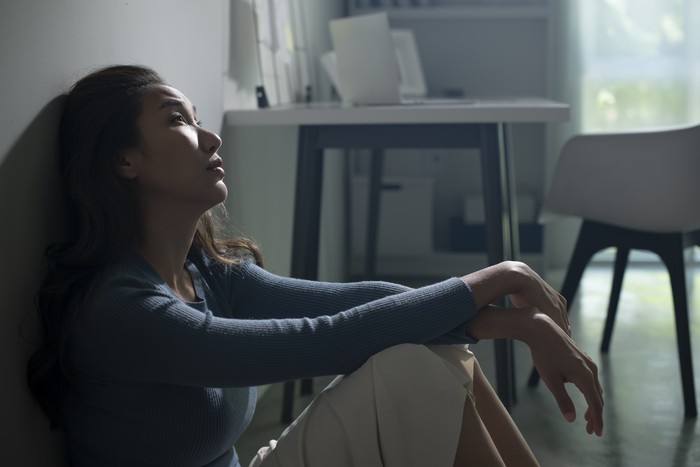 Young Asian woman sitting on floor at home feeling sad tired and worried suffering depression in mental health, problems and broken heart concept, life difficulties