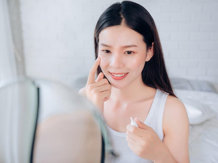Mirror reflection of woman with skincare cream, spa lotion or dermatology ointment for melasma or acne treatment. Bathroom facial routine, healthcare and face of girl apply cosmetics beauty product