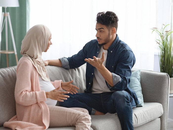 Pregnancy And Relationship Problems. Pregnant Muslim Spouses Arguing At Home, Expectant Muslim Lady In Hijab And Her Arab Husband Quarreling While Sitting On Couch In Living Room, Free Space