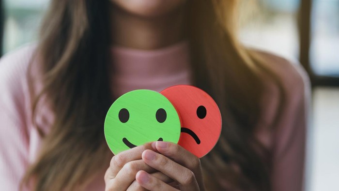 Woman Hands holding sad face hiding or behind happy smiley face, bipolar and depression, mental health concept, personality, mood change, therapy healing split concept.