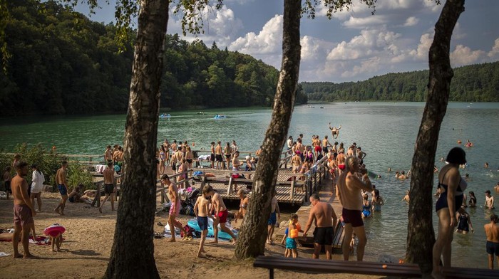 People enjoy the warm weather by a lake near Vilnius, Lithuania, Thursday, Aug. 17, 2023. The heat wave continues in Lithuania as temperature rise to as high as 32 degrees Celsius (89.6 degrees Fahrenheit). (AP Photo/Mindaugas Kulbis)