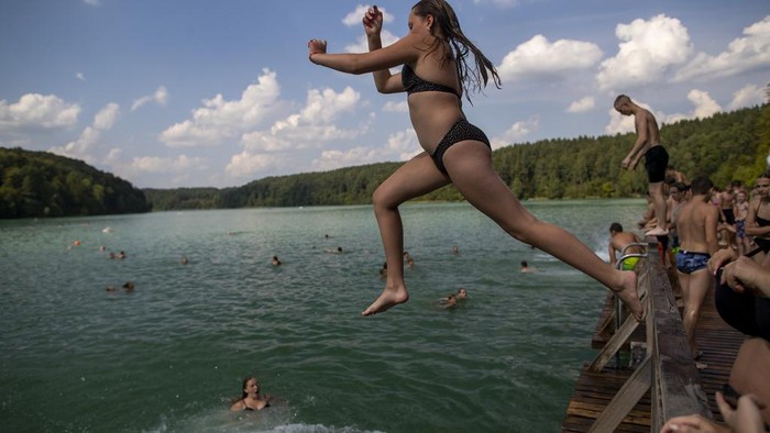 People enjoy the warm weather by a lake near Vilnius, Lithuania, Thursday, Aug. 17, 2023. The heat wave continues in Lithuania as temperature rise to as high as 32 degrees Celsius (89.6 degrees Fahrenheit). (AP Photo/Mindaugas Kulbis)