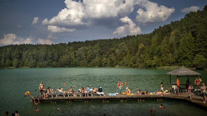 People enjoy the warm weather by a lake near Vilnius, Lithuania, Thursday, Aug. 17, 2023. The heat wave continues in Lithuania as temperature rise to as high as 32 degrees Celsius (89.6 degrees Fahrenheit). (AP Photo/Mindaugas Kulbis)