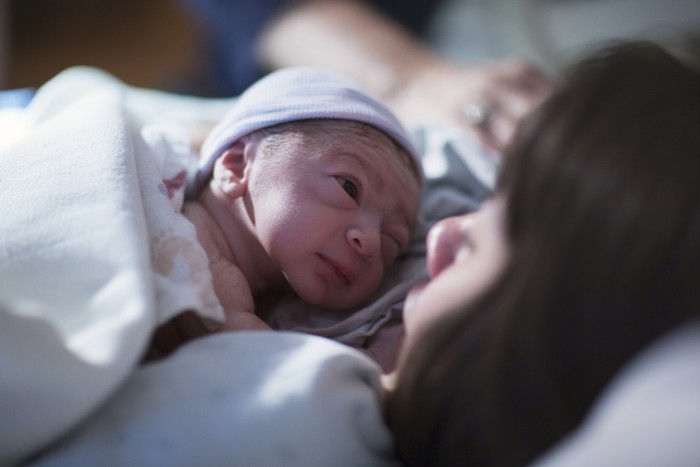 Pregnant young woman lying on the bed in delivery room. Side view of happy pregnant female resting on bed in hospital ward. Healthcare and pregnancy concept