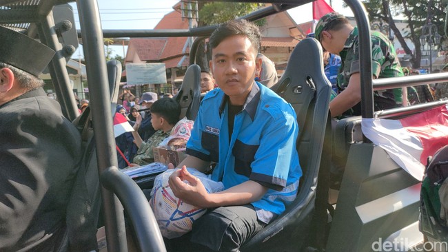 Kemeja Gibran hadir dalam warna biru dengan aksen hitam, lengkap beratribut nama ‘Mas Gibran dan Petugas Parkir di pundak. Kancingnya dibiarkan terbuka sehingga terekspos kaus hitam di baliknya. Adapun celana kargo jadi andalan untuk bawahan. (Foto: Tara Wahyu NV/detikJateng)