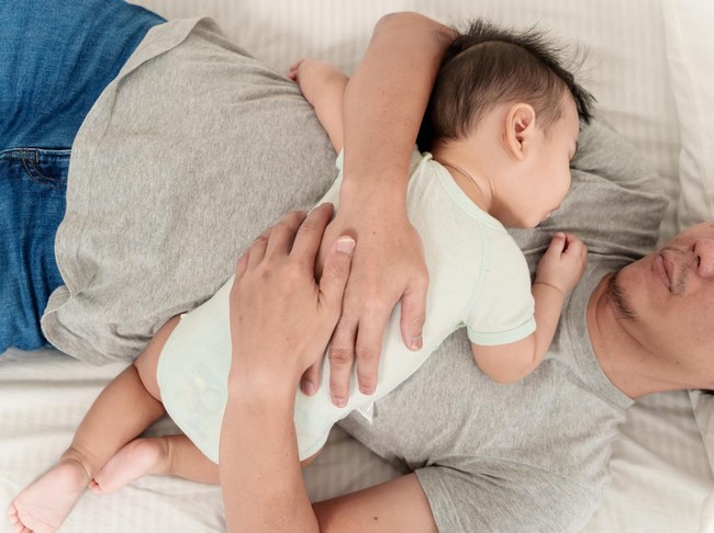 Top view of cute Asian baby boy sleeping on his fathers chest. Asian father and baby sleeping together at home, father holding and embracing his son in arms.