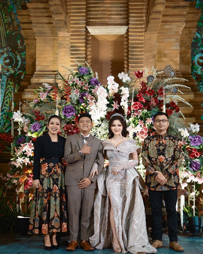 Untuk sesi kedua, Denny dan Bella berganti busana dengan tema modern. Mempelai pria mengenakan setelan jas abu-abu, sementara mempelai wanita tampil glamor berbalut gaun warna silver dan tiara. Foto: Instagram/@showimah