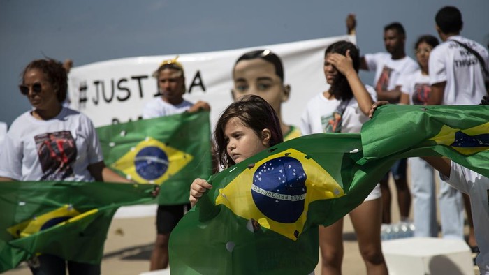 Protes Kekerasan, Belasan Peti Mati Berjejer di Pantai Copacabana Brasil Brazilian national flag punctured with holes to represent children killed by stray bullets are draped over coffins as part of a protest calling for an end to the violence that erupts during police operations in the favelas against suspected drug traffickers and thieves, on Copacabana beach in Rio de Janeiro, Brazil, Saturday, Aug. 19, 2023. (AP Photo/Bruna Prado)